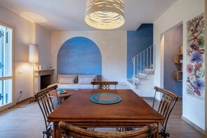 A dining area with a wooden table, wicker chairs, a blue wall with an arched design, a staircase, and a wall-mounted light fixture. - Villa Tigli: A 5-Minute Walk From the Beach by Top Villas Sardinia (Quartu Sant'Elena)