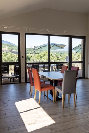 A dining area with a table and chairs, large windows with a view of greenery and mountains, and a wooden floor. - 6-Bedroom Vacation Rental - ALTER ET GO! Vacation Rental Village - Panoramic view (MARQUIXANES)