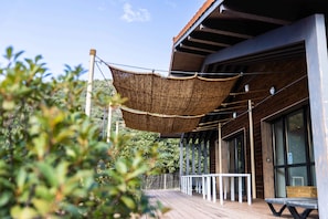 A wooden deck with a hanging shade, a white railing, and a building with large windows. - 6-Bedroom Vacation Rental - ALTER ET GO! Vacation Rental Village - Panoramic view (MARQUIXANES)