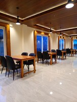 A spacious dining area with wooden tables and chairs, large windows, and a polished floor.