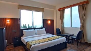 Hotellihuone, jossa on suuri sänky, työpöytä ja kaksi tuolia. Huoneessa on ikkunat, joissa on verhot, ja katossa on puupaneelista tehty koristeellinen kuvio.