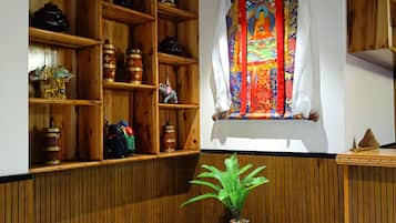 Una habitación con estanterías de madera, un ventanal con un tapiz colorido y una pequeña mesa de madera con una planta.