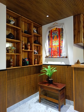 A room with wooden shelving, a window with a colorful tapestry, and a small wooden table with a plant. - Sunhill Ravangla Retreat (Ravangla)