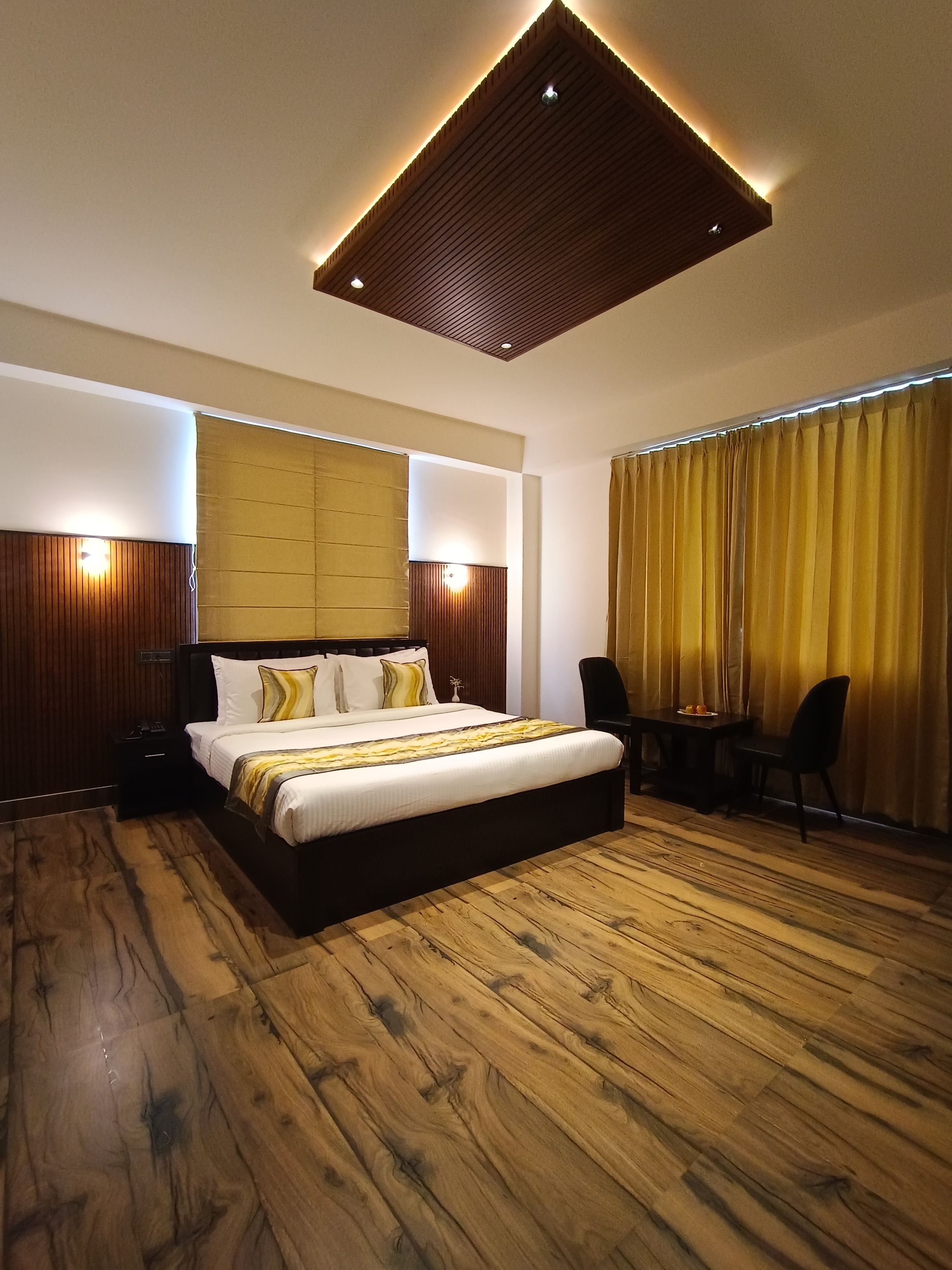 Una habitación de hotel moderna con una cama grande, suelo de madera, un escritorio con sillas y una lámpara en el techo.