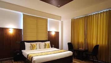 Una habitación de hotel moderna con una cama grande, suelo de madera, un escritorio con sillas y una lámpara en el techo.