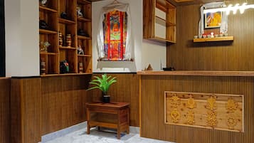 Een kamer met houten lambrisering, een marmeren vloer, een plank met decoratieve objecten, een potplant en een wandplank met een ingelijst beeld.