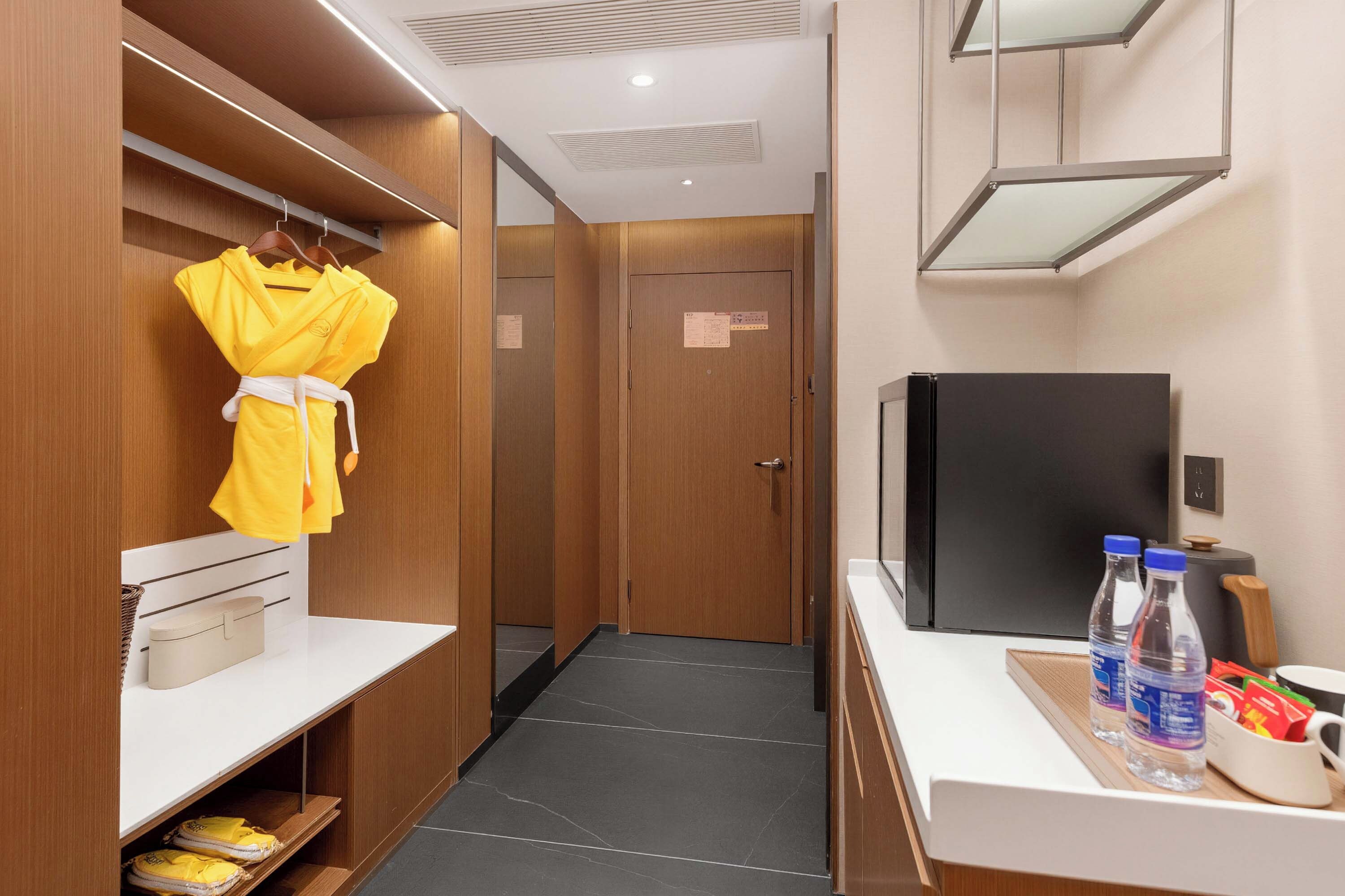 A hotel room with a wardrobe, a mirror, a television, and a tray with bottled water and snacks.