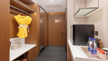 A hotel room with a wardrobe, a mirror, a television, and a tray with bottled water and snacks.