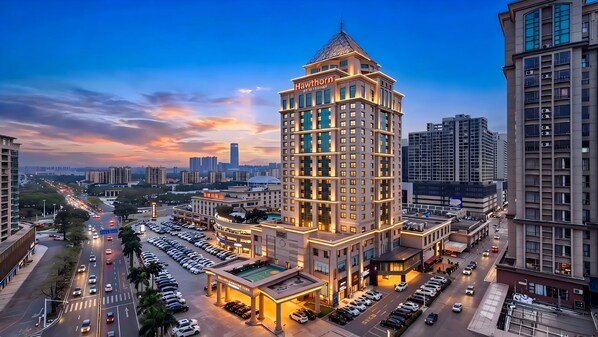 A multi-story hotel with a prominent corner tower, surrounded by a parking lot and other buildings.