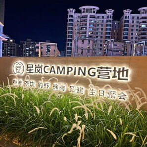 A sign for '星岗CAMPING营地' with a view of modern buildings in the background.
