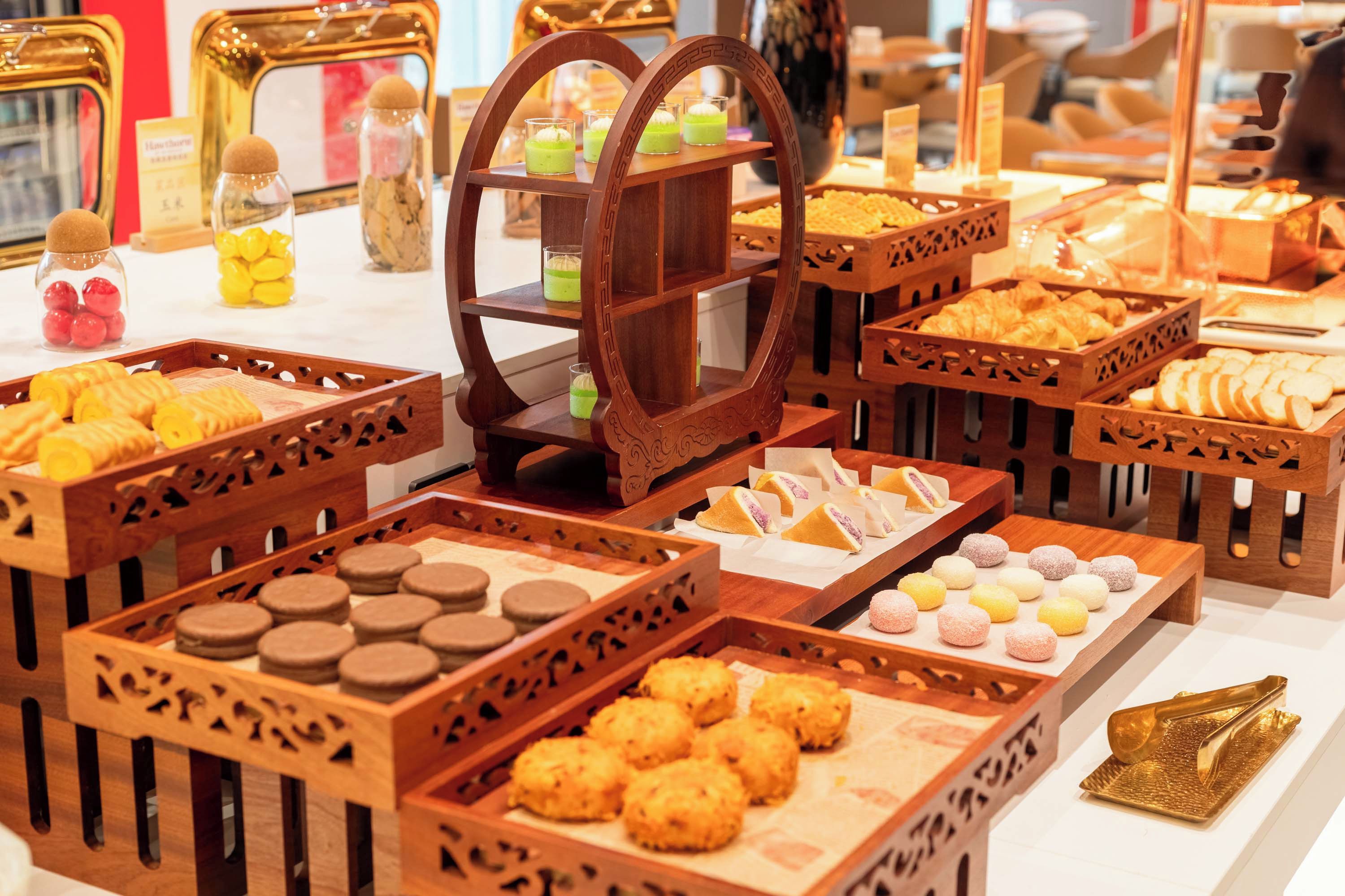 A variety of food items displayed in wooden crates and a central wooden stand with multiple glasses of beverages.
