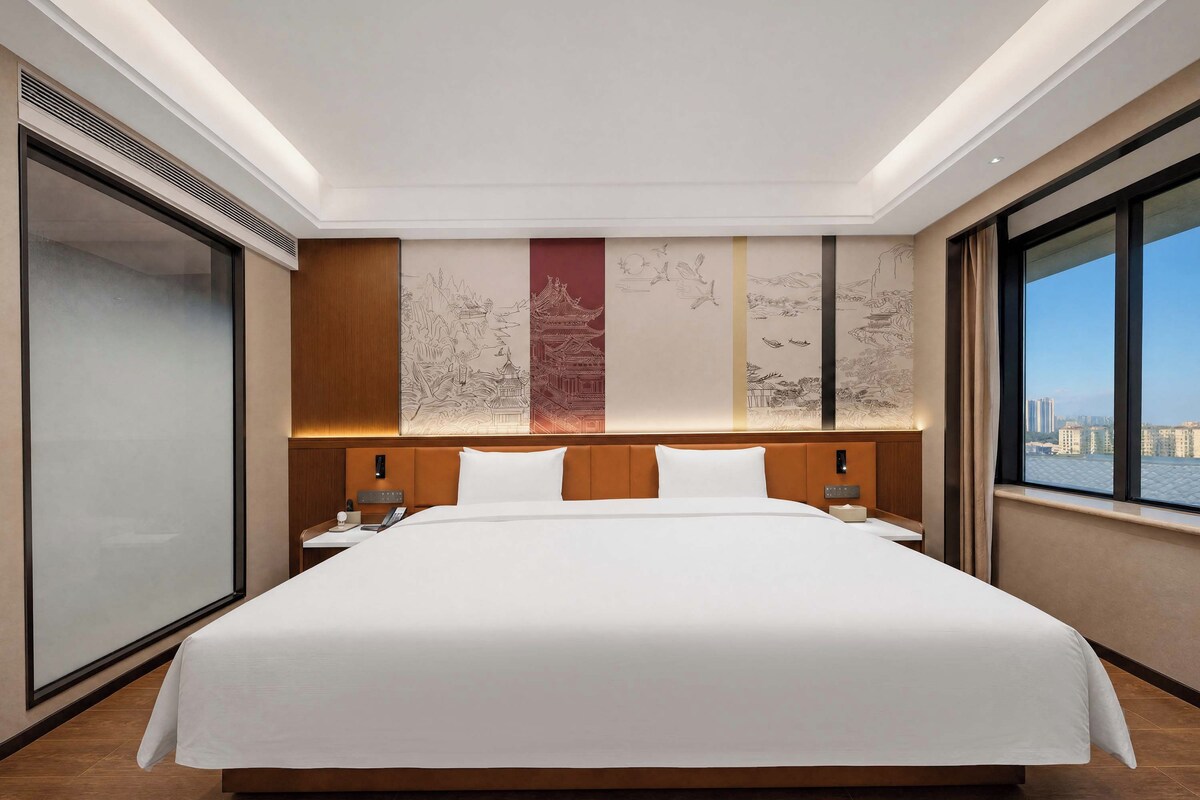 Une chambre d’hôtel avec un grand lit, une vue sur la ville et un mur décoré d’œuvres d’art.