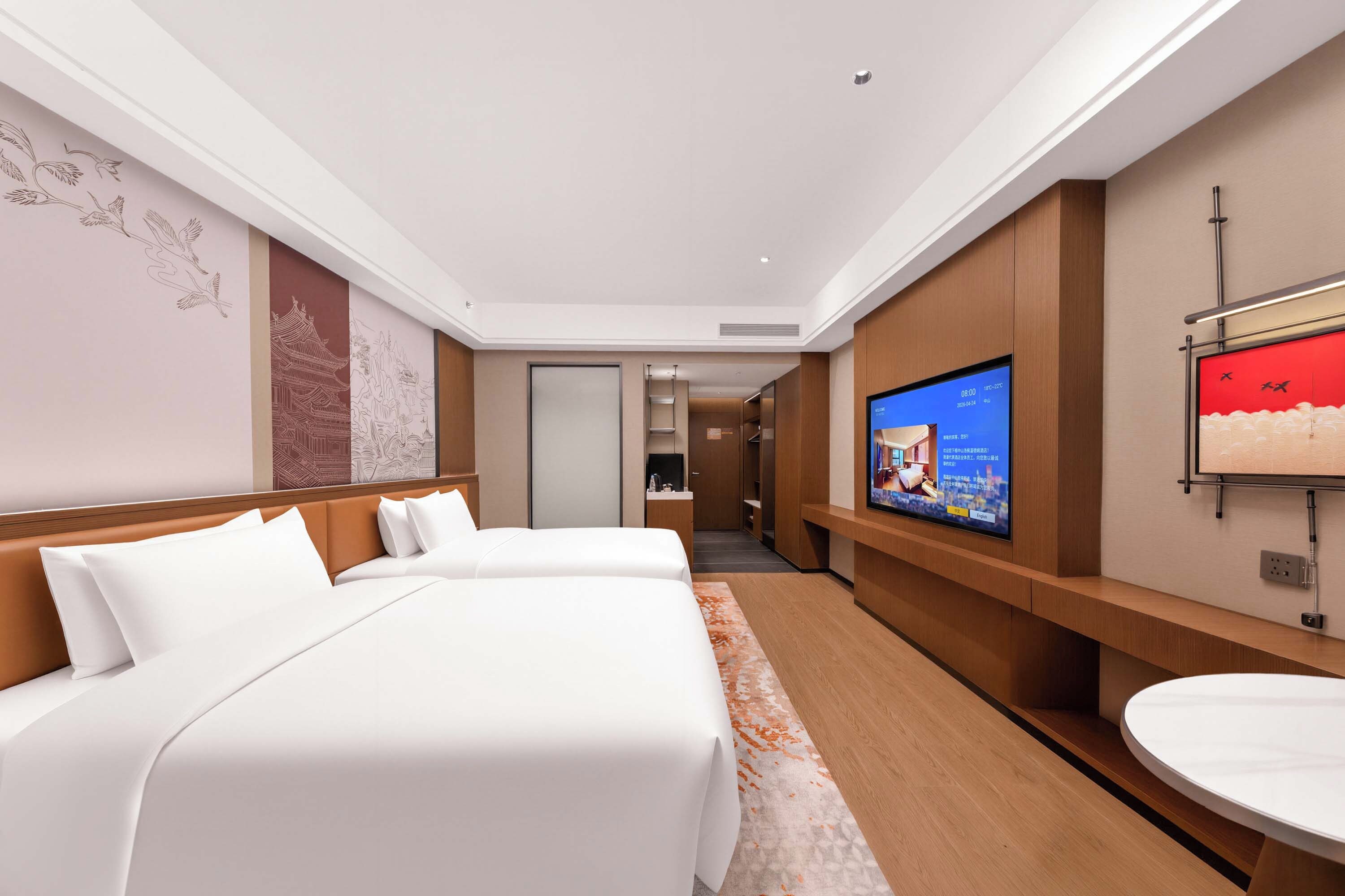 Habitación de hotel con dos camas, un televisor, un baño con lavamanos y un pasillo que conduce a otro baño.