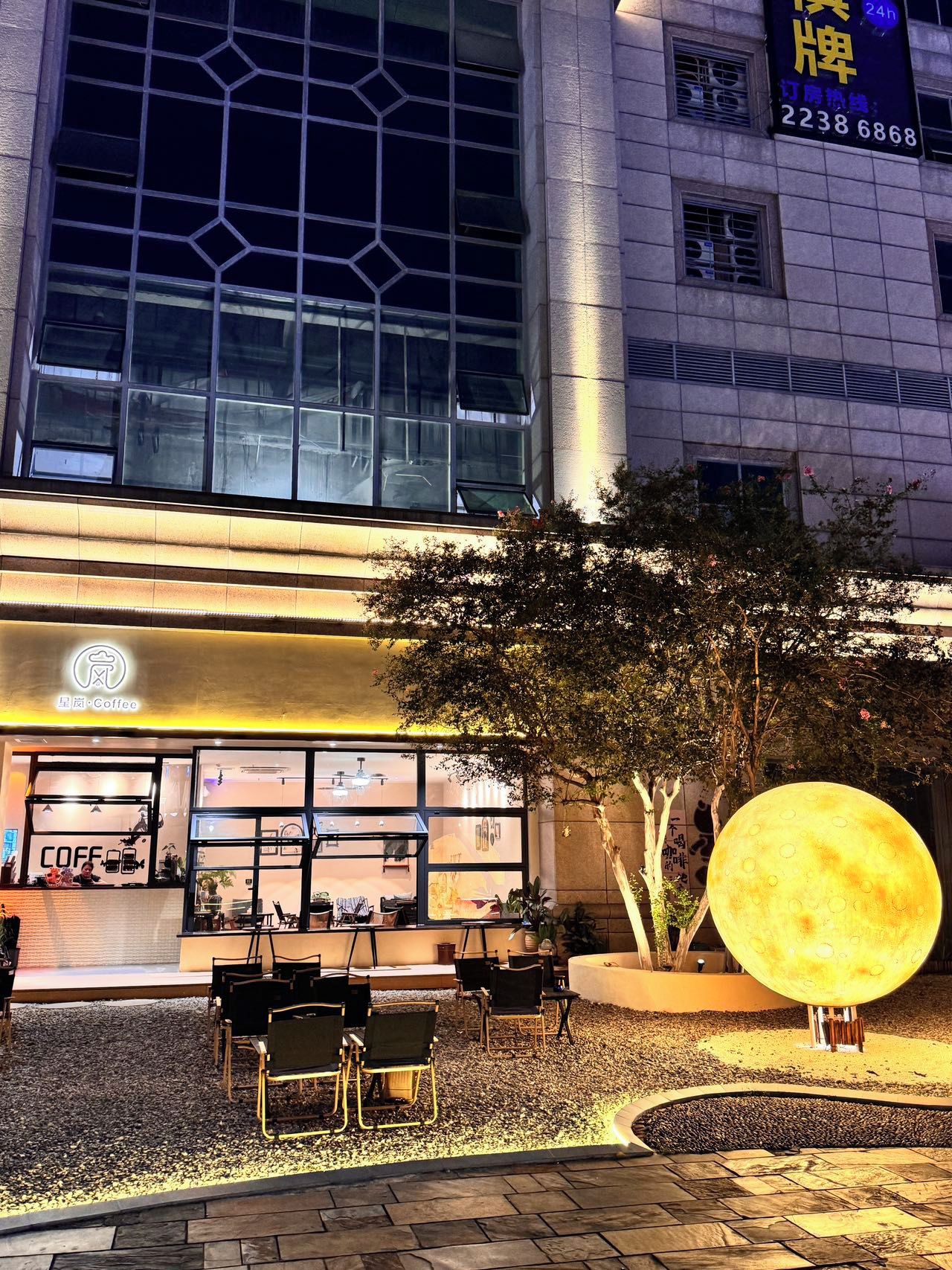 A coffee shop with outdoor seating and a large illuminated moon sculpture.