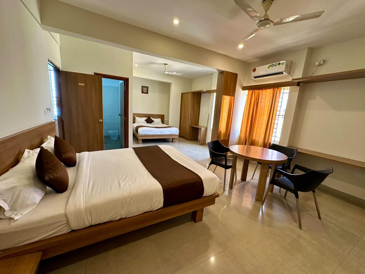 Une chambre d’hôtel avec un lit, un bureau et des chaises. Elle est équipée d’un ventilateur de plafond et d’un appareil de climatisation.