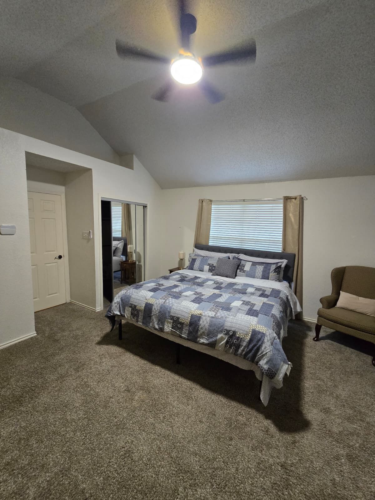 A bedroom with a bed, a ceiling fan, a window with curtains, and a door.