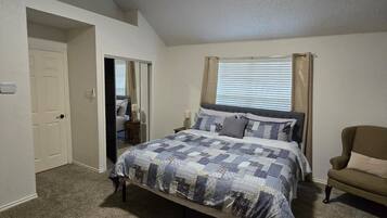 A bedroom with a bed, a ceiling fan, a window with curtains, and a door.