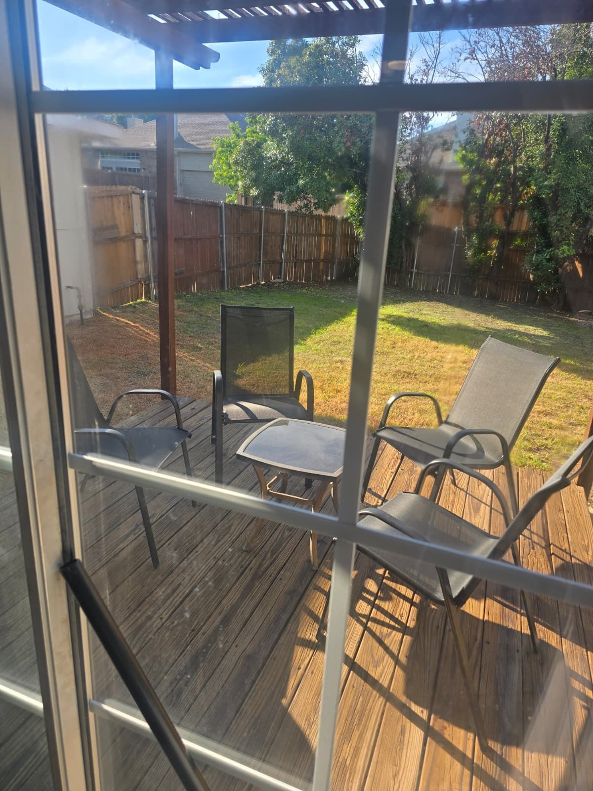 A deck with outdoor furniture, including chairs and a table, overlooking a backyard with a wooden fence and trees.