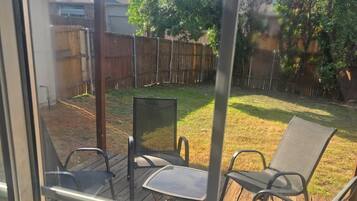 A deck with outdoor furniture, including chairs and a table, overlooking a backyard with a wooden fence and trees.