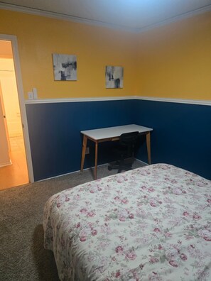 Ein Schlafzimmer mit einem Bett, einem Schreibtisch und zwei an der Wand befestigten Kunstwerken.