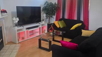 A living room with a black sofa, a flat-screen TV, a potted plant, and a window with curtains.