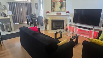 A living room with a black sofa, a television, a fireplace, and a dining area with chairs and a table.