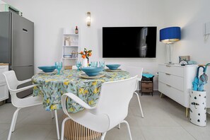 Cozinha moderna com armários brancos, uma mesa de jantar posta com tigelas e copos azuis, e uma TV de tela plana fixada na parede.