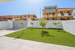 A rooftop terrace with artificial grass, a gated entrance, and residential buildings in the background. - Villa Smeraldo e Arancia Valledoria Sardinia (Valledoria)