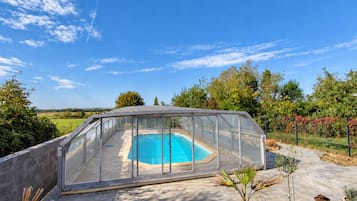 Una piscina con cerramiento de vidrio, rodeada de plantas en macetas y un cielo despejado.