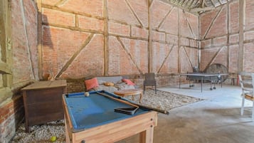 Una mesa de billar en una habitación con paredes de ladrillo y suelo de hormigón.