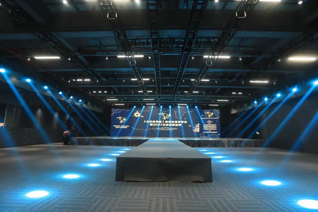An indoor venue with a stage, a large screen displaying text, and a patterned carpet.