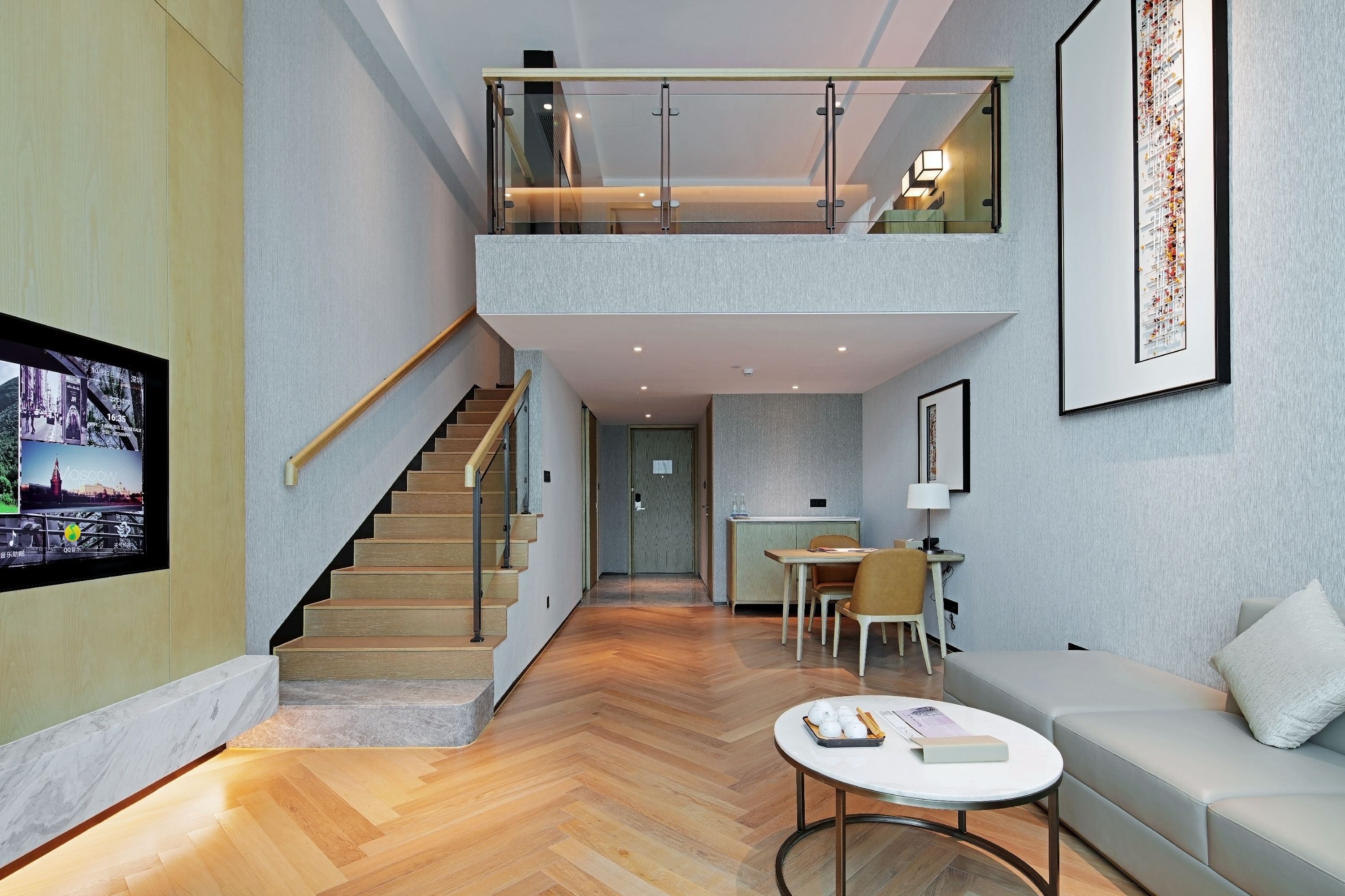 Un intérieur moderne avec un escalier menant à une mezzanine, un coin repas et un espace de vie comprenant un canapé et une table basse.