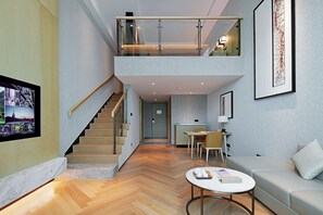 Un interior modern amb una escala que condueix a un altell, una zona de menjador i un espai de estar amb un sofà i taula de centre.
