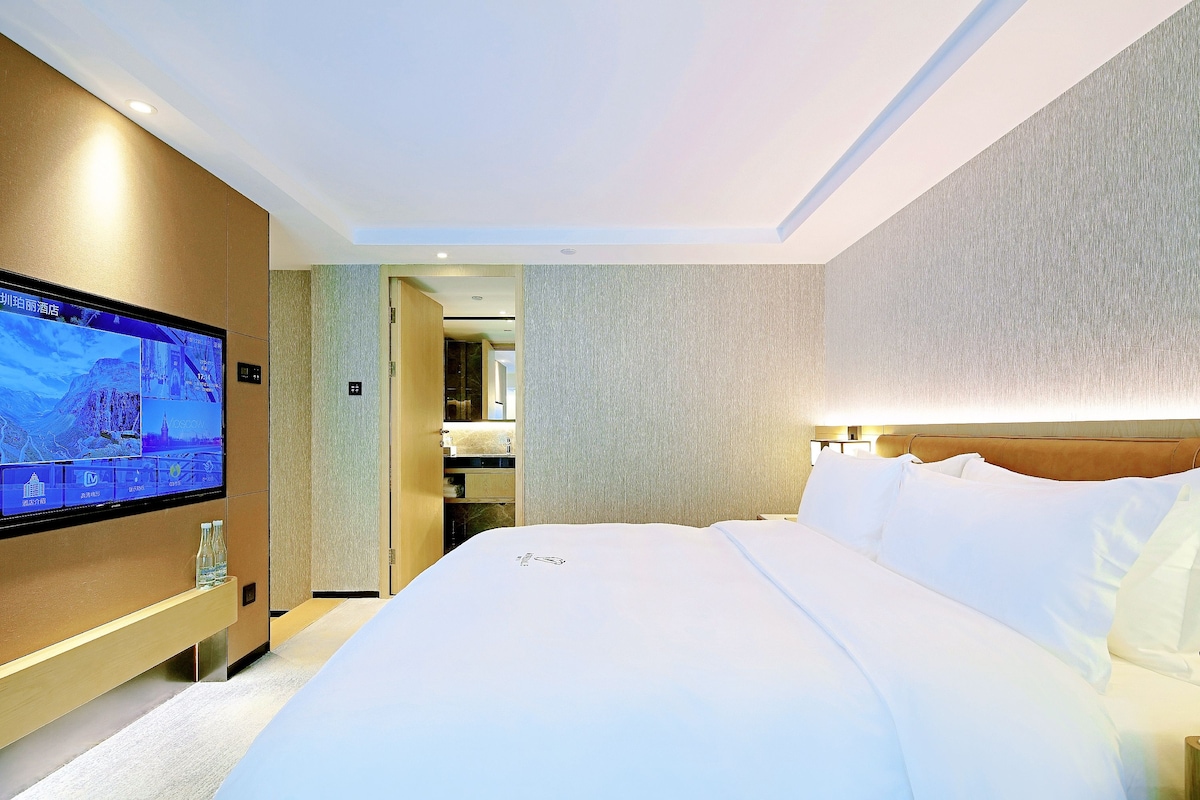 A hotel room with a large bed, a television on the wall, and a bathroom visible through an open door.