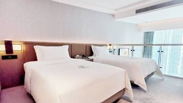 A hotel room with two beds, a nightstand, a wall-mounted lamp, and a large window with curtains.
