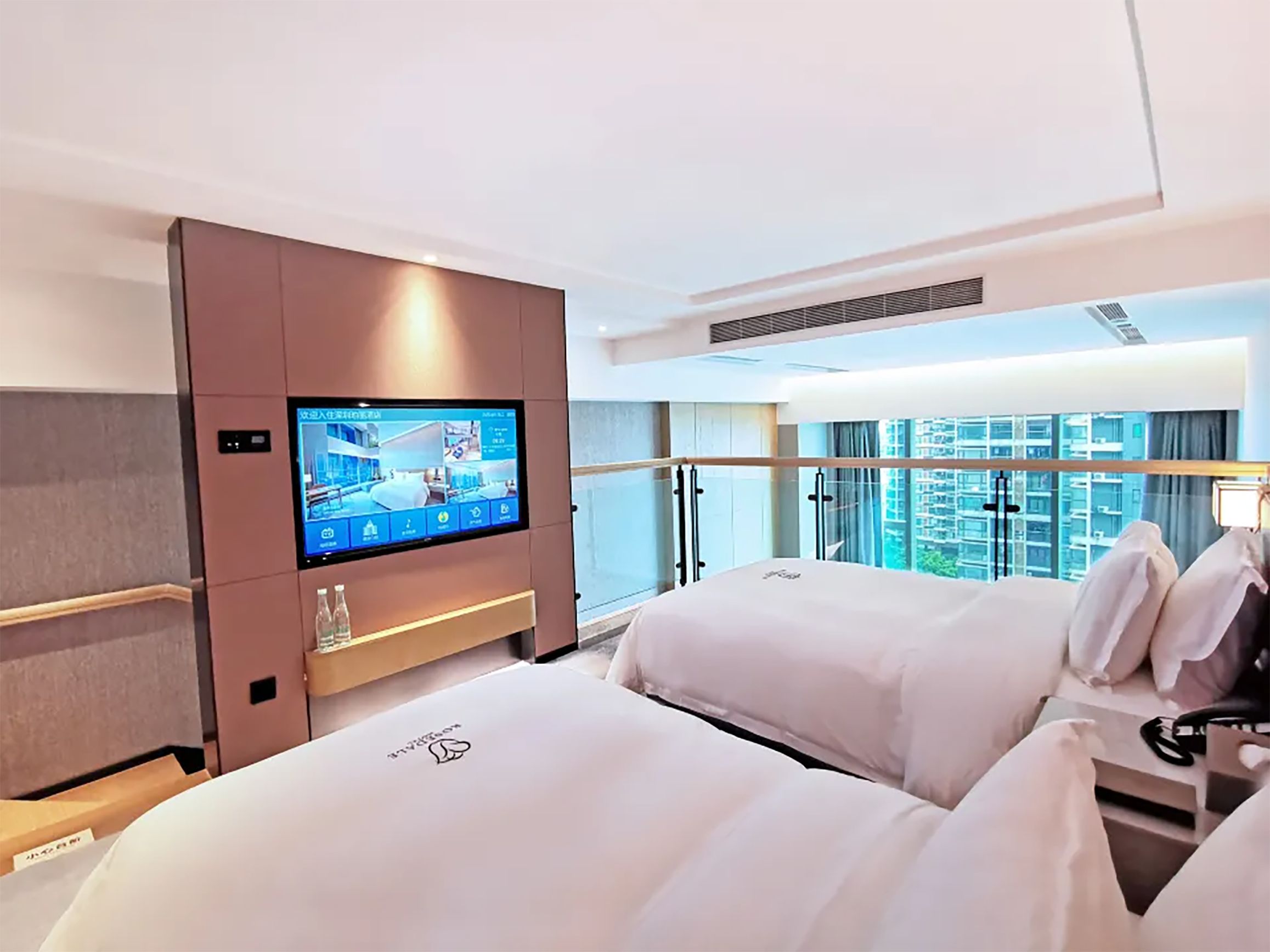 A hotel room with a large bed, a television mounted on the wall, and a view of the cityscape through the window.