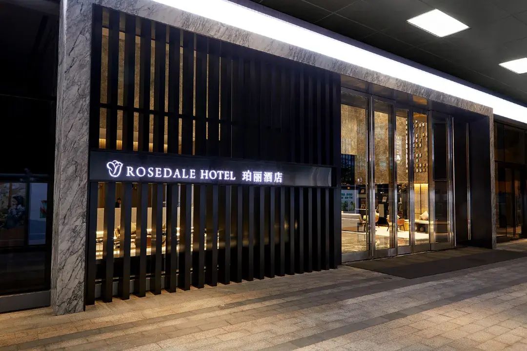 Een hotelentree met een moderne gevel, grote glazen deuren en een bord waarop staat ROSEDALE HOTEL.