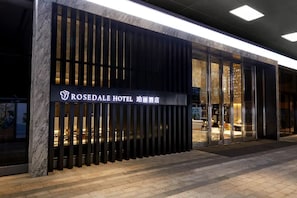 A hotel entrance with a modern facade, large glass doors, and a sign indicating it's the ROSEDALE HOTEL.