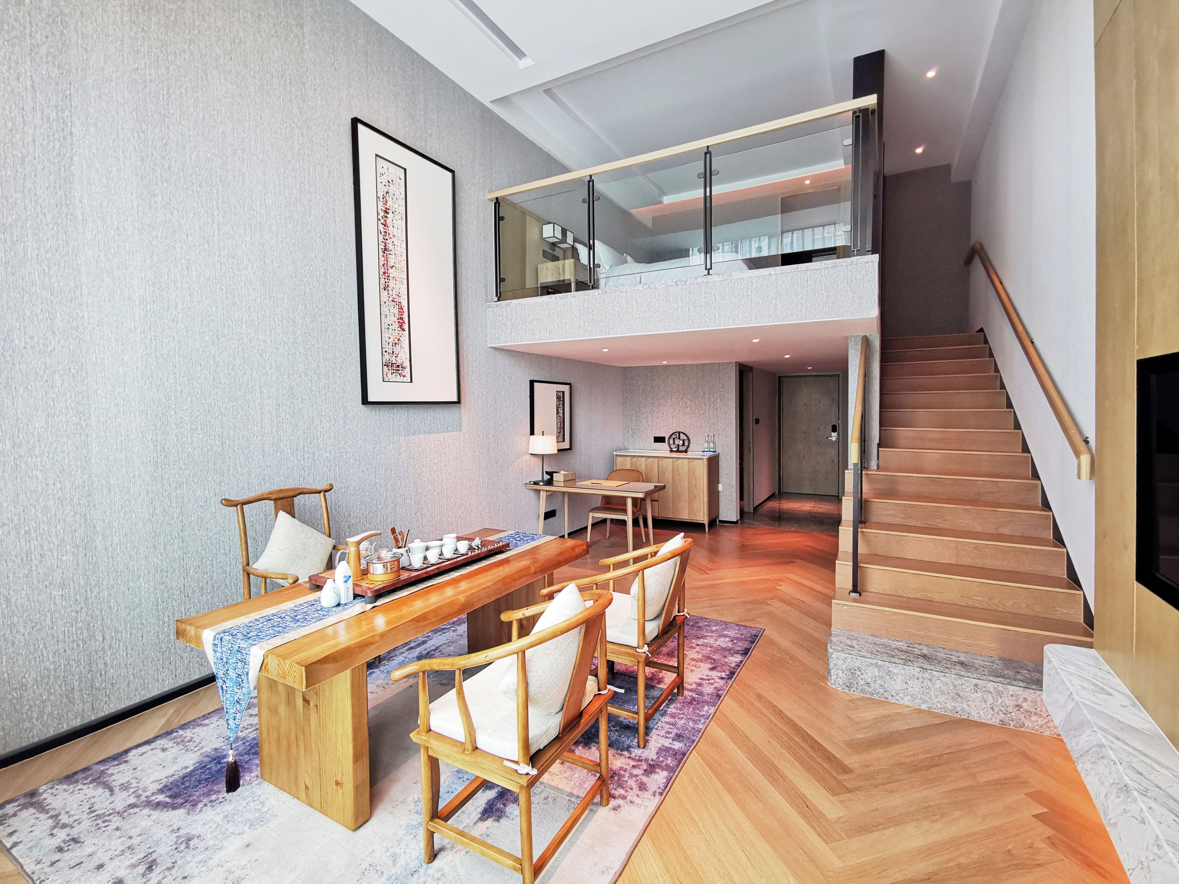 Un interior moderno con zona de comedor, muebles de madera, una escalera y un entresuelo.