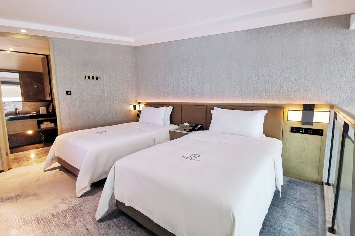 A hotel room with two beds, a minibar, a mirror, and a control panel.