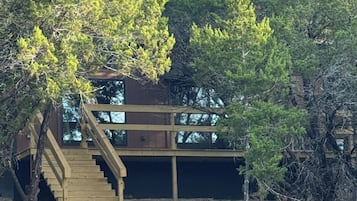 Una cabaña de madera con una escalera que lleva a una terraza, rodeada de árboles.