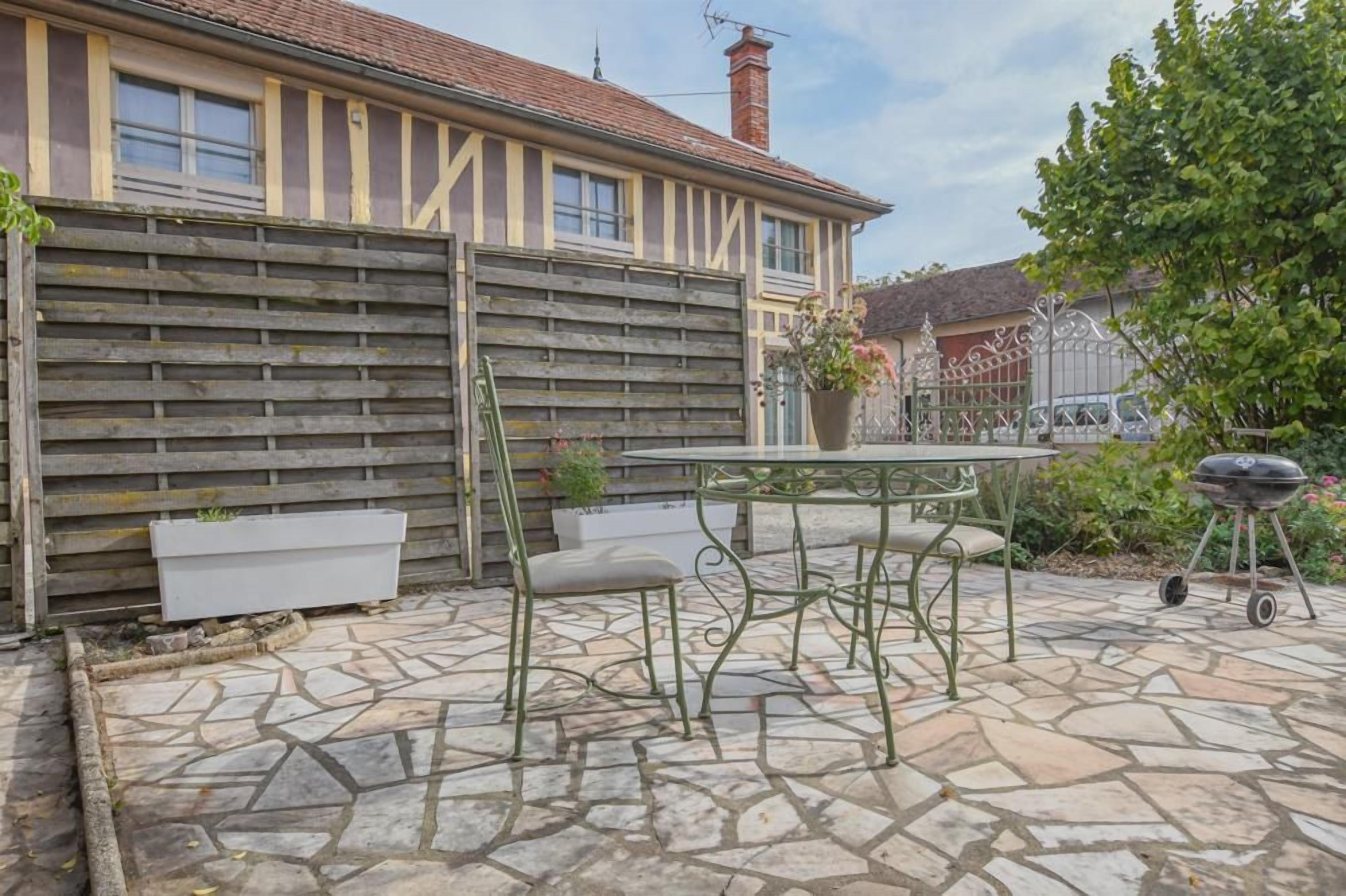 Een terras met een stenen vloer, een metalen tafel en een barbecue.