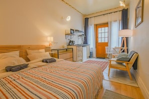 Een hotelkamer met een bed, een bureau, een stoel, een lamp en een deur naar een balkon.