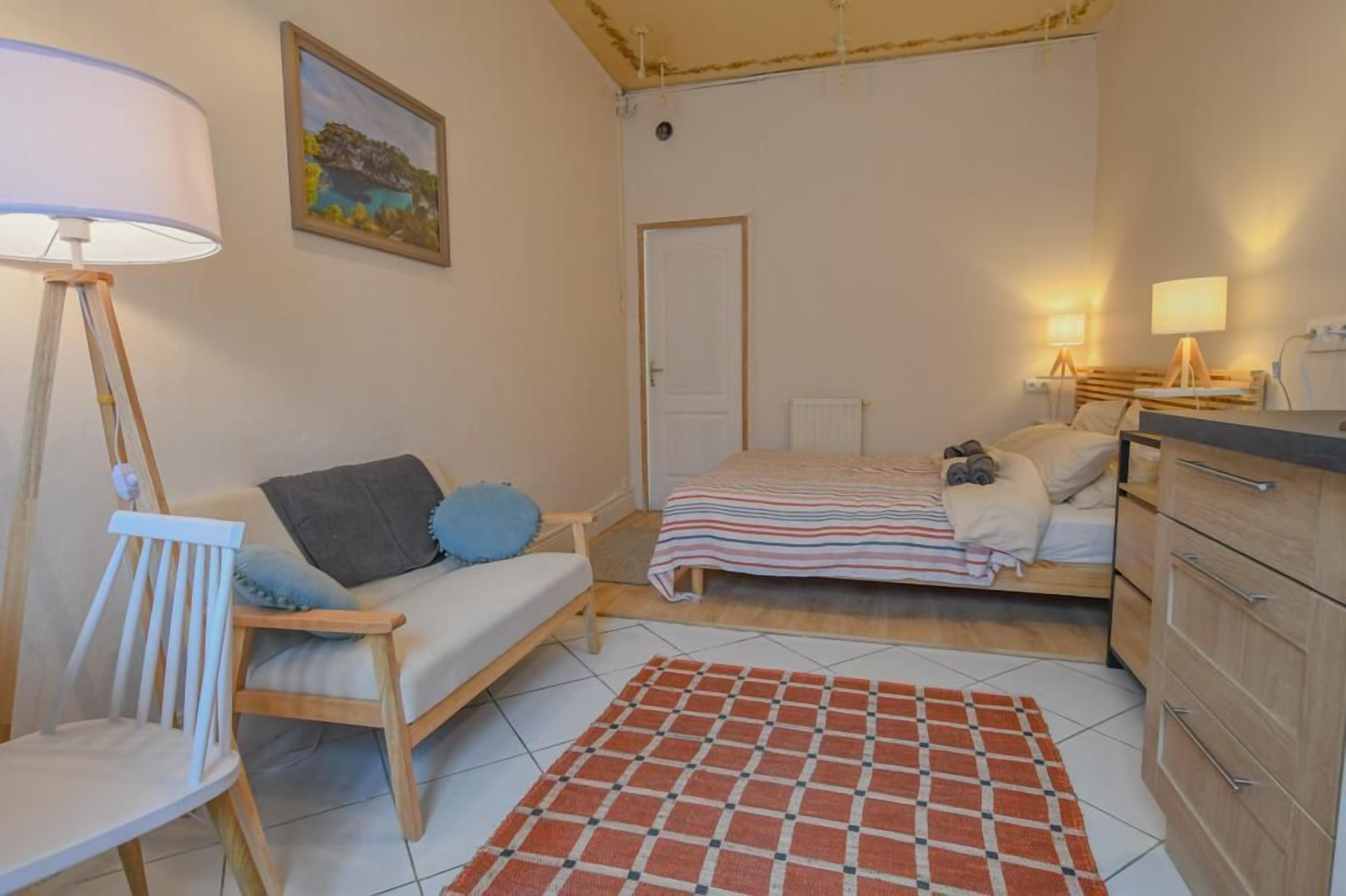 Un dormitorio con cama, mesitas de noche, una silla, una lámpara y un cuadro en la pared.