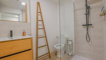 Badeværelse med en træstige, toilet, brusebad og et spejl.