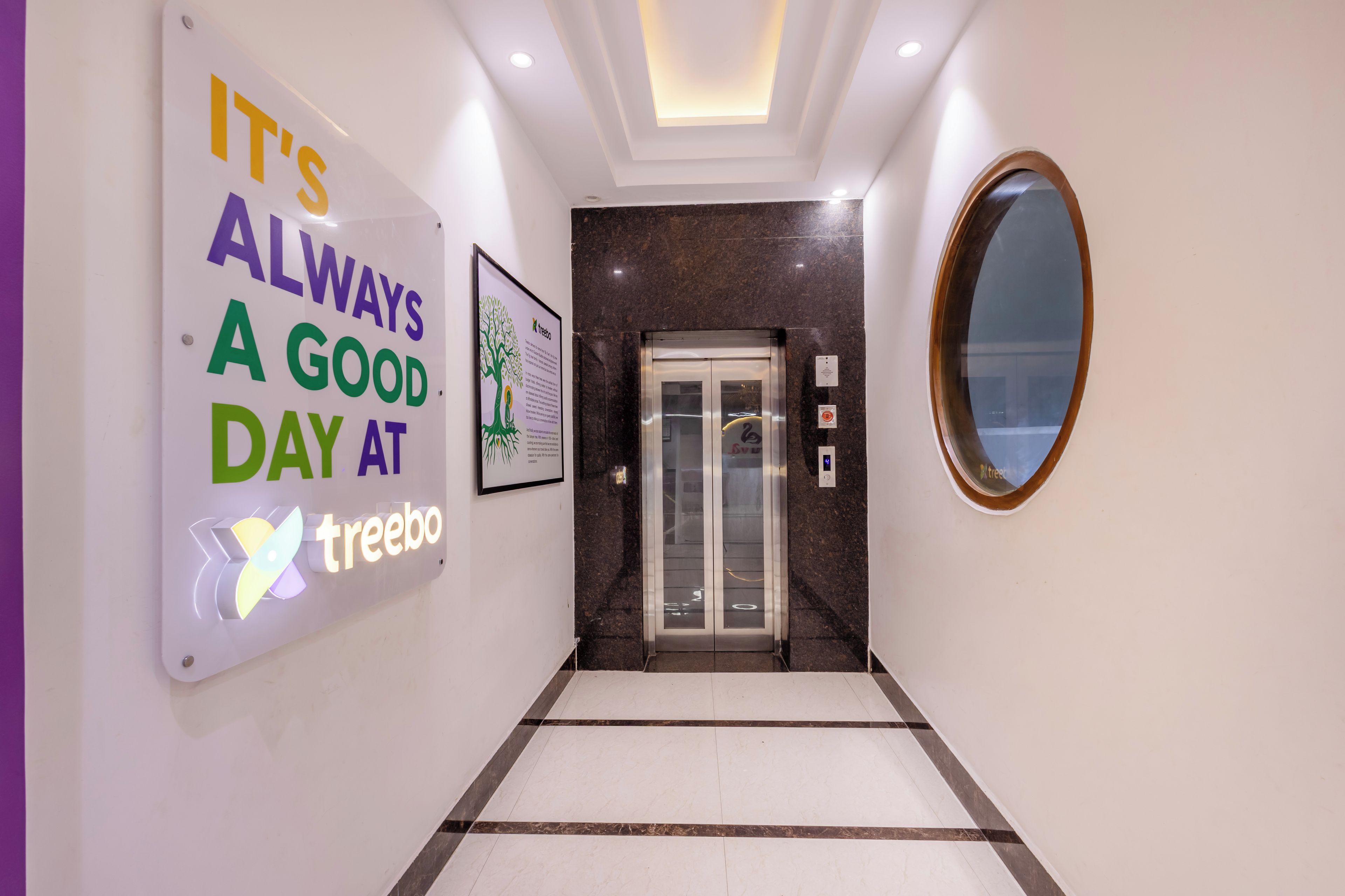 A hallway with a sign that reads 'IT'S ALWAYS A GOOD DAY AT treebo,' an elevator, and a mirror on the wall.