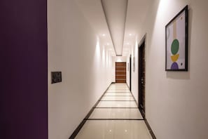 A hallway with a tiled floor, a wooden door at the end, and a framed artwork on the wall. - Treebo Premium Truva (Faridabad)