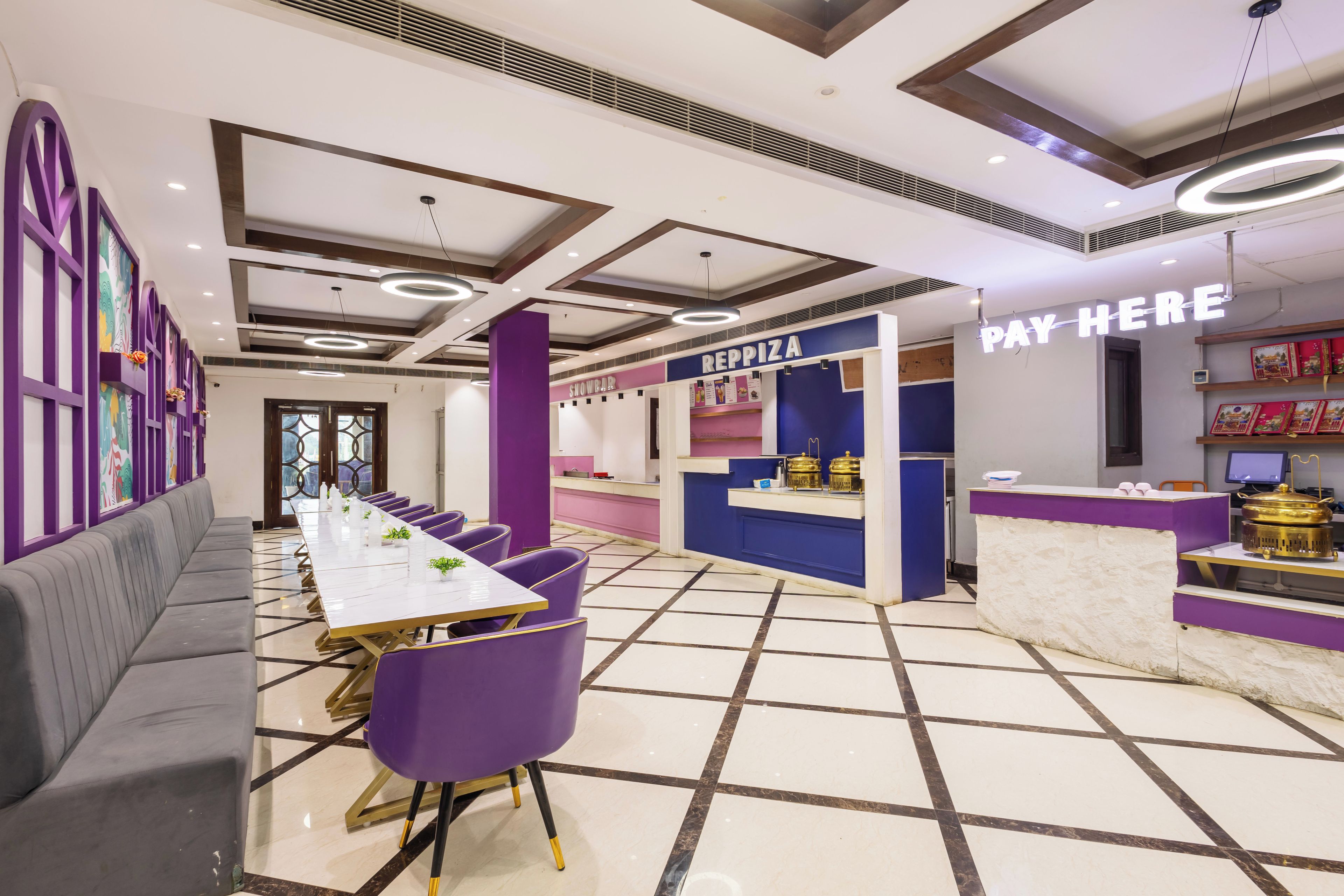 A modern interior with a long dining table, purple chairs, and a counter labeled 'PAY HERE'.