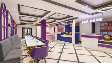 A modern interior with a long dining table, purple chairs, and a counter labeled 'PAY HERE'.