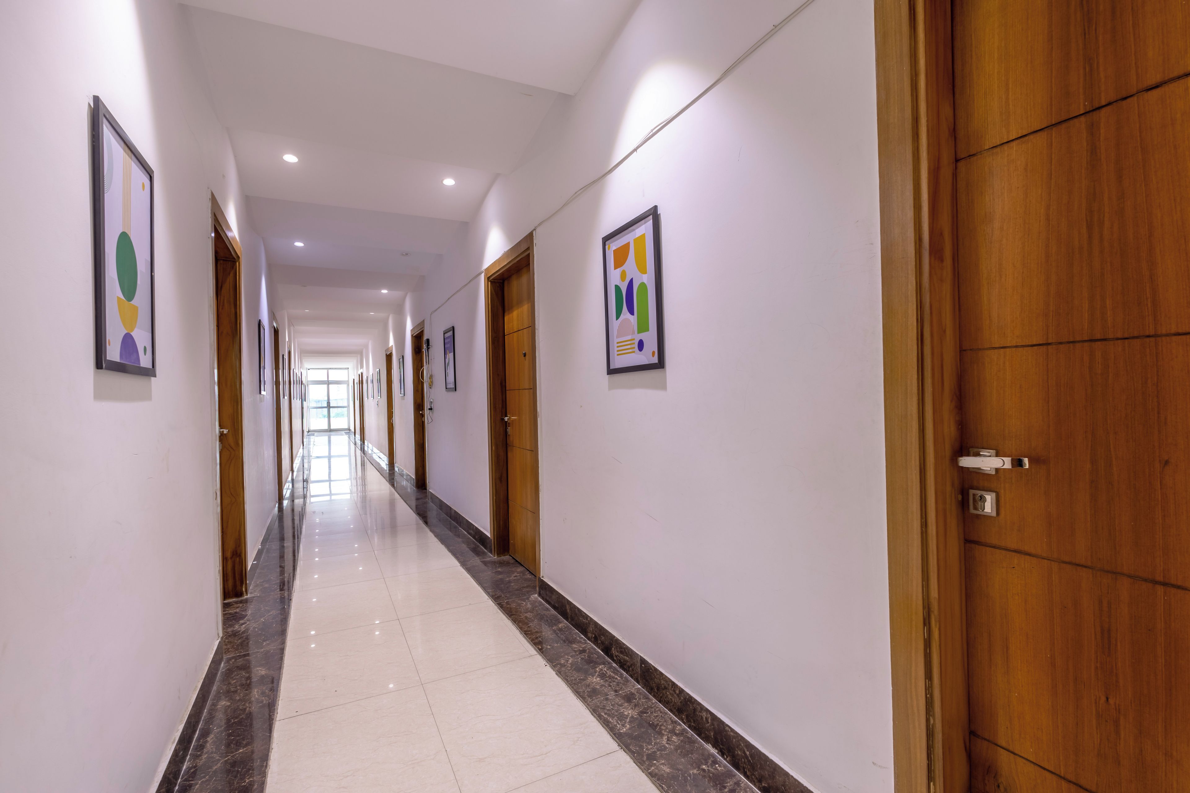 Un pasillo de hotel con puertas de madera, obras de arte enmarcadas en las paredes y suelo de baldosas.